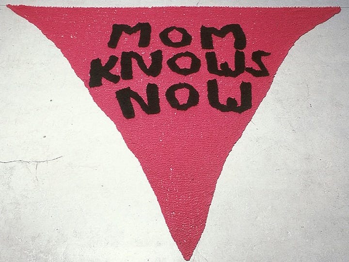 1) The 'Mom Knows Now' banner is seen hanging from a tall church steeple, hanging right in front of the bell speakers, and above a clock. The building mostly consists of brown brick, with white architecture at the top, where the banner is hanging. 2) A close-ip image of the 'Mom Knows Now' banner against a white background. The banner is pink/red with black text, and it is in the shape of a triangle.