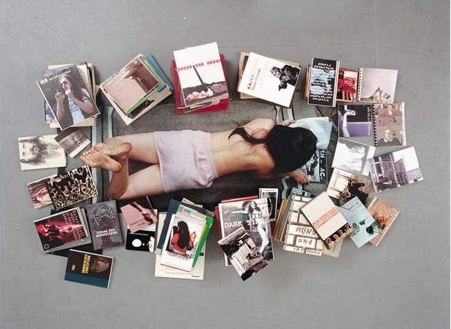 This may contain: a woman laying on the ground surrounded by many books