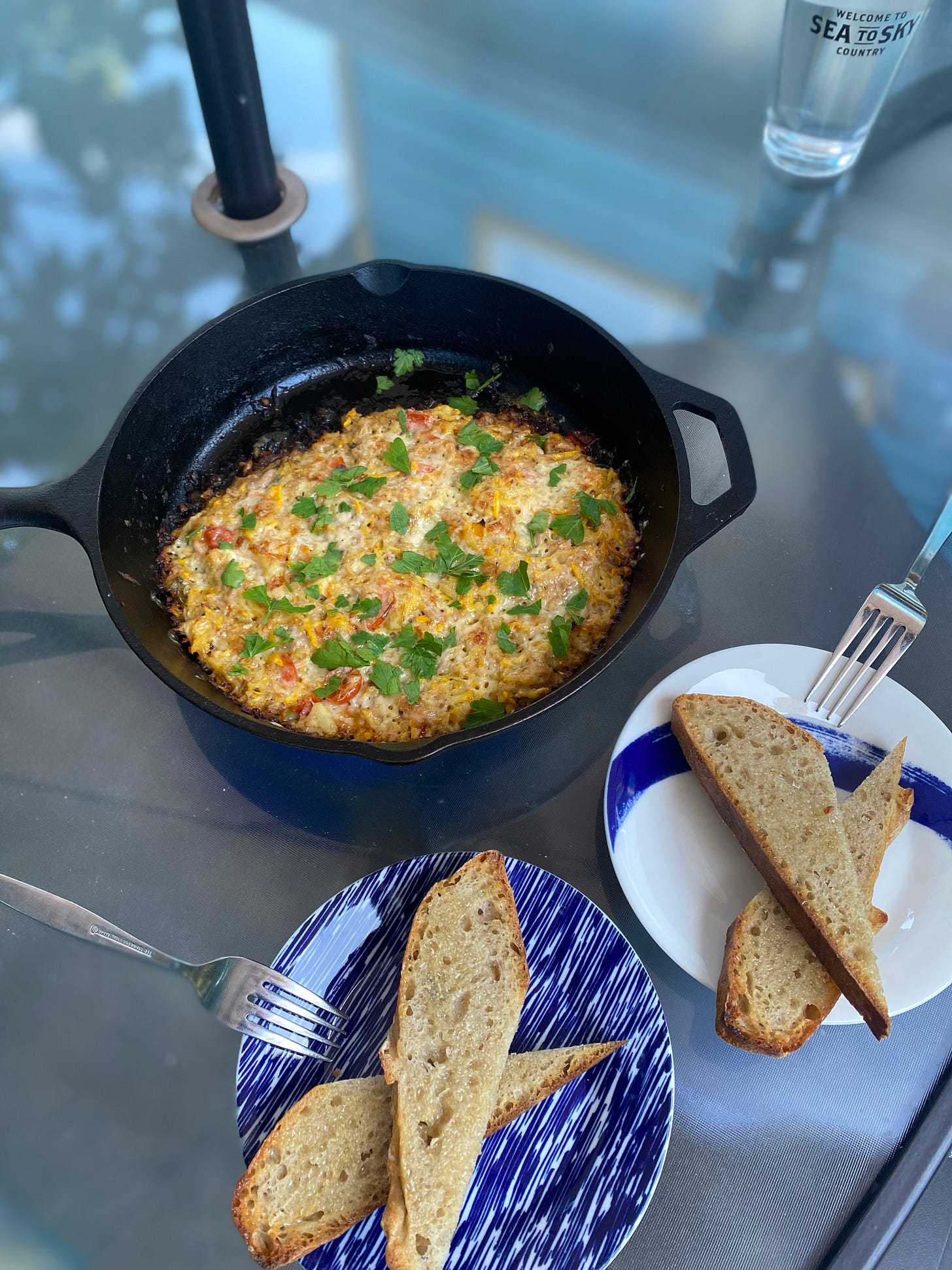 A cast iron pan of the tuna & zucchini casserole described above, sprinkled with roughly chopped parsley. On two side plates are diagonally cut slices of toast.