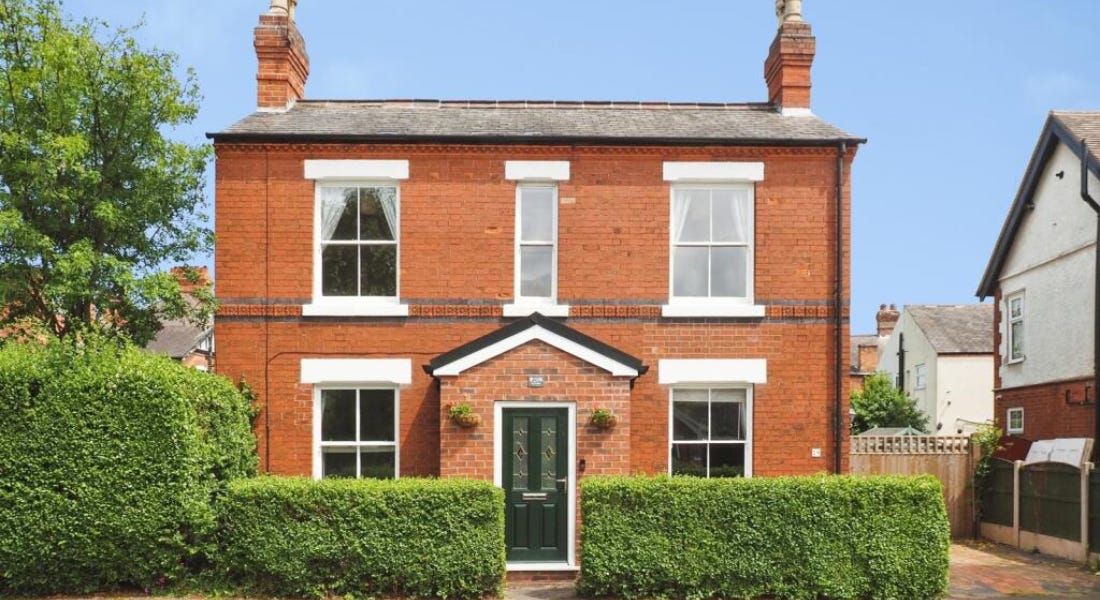 A brick house with windows, a dark green door, and a hedge in front of it A brick house with windows, a dark green door, and a hedge in front of it