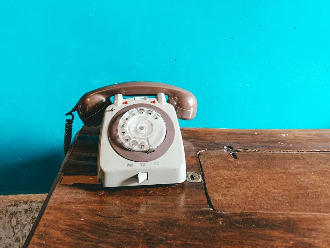 white and gray rotary phone on brown surface white and gray rotary phone on brown surface