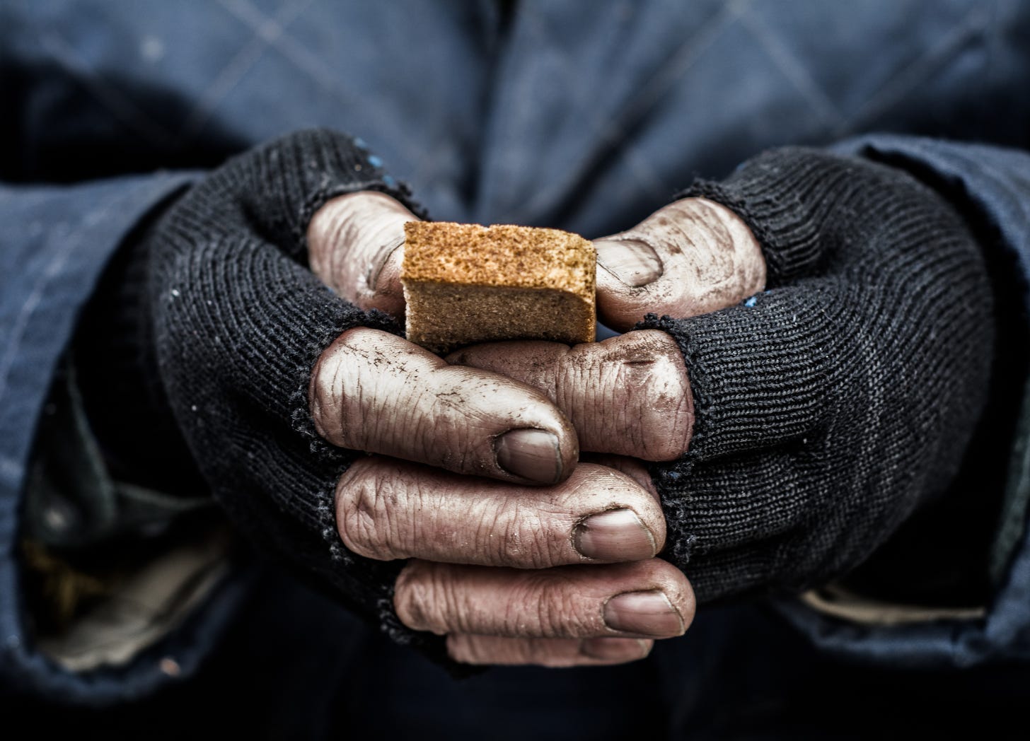 Dirty hands tightly clamping a piece of bread, symbolizing survival and need, highlighting the moral dilemma of spending on beauty in a world of suffering.