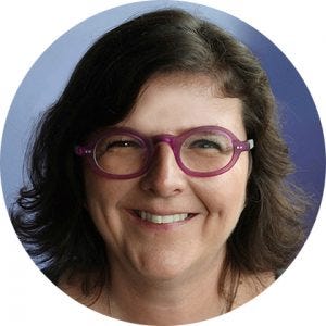 Mulher de cabelos castanhos na altura do ombro. Ela sorri para a foto e usa óculos roxos. Mulher de cabelos castanhos na altura do ombro. Ela sorri para a foto e usa óculos roxos.