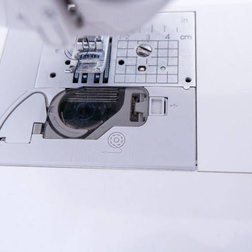 a bobbin with thread next to the bobbin compartment on a top loading sewing machine