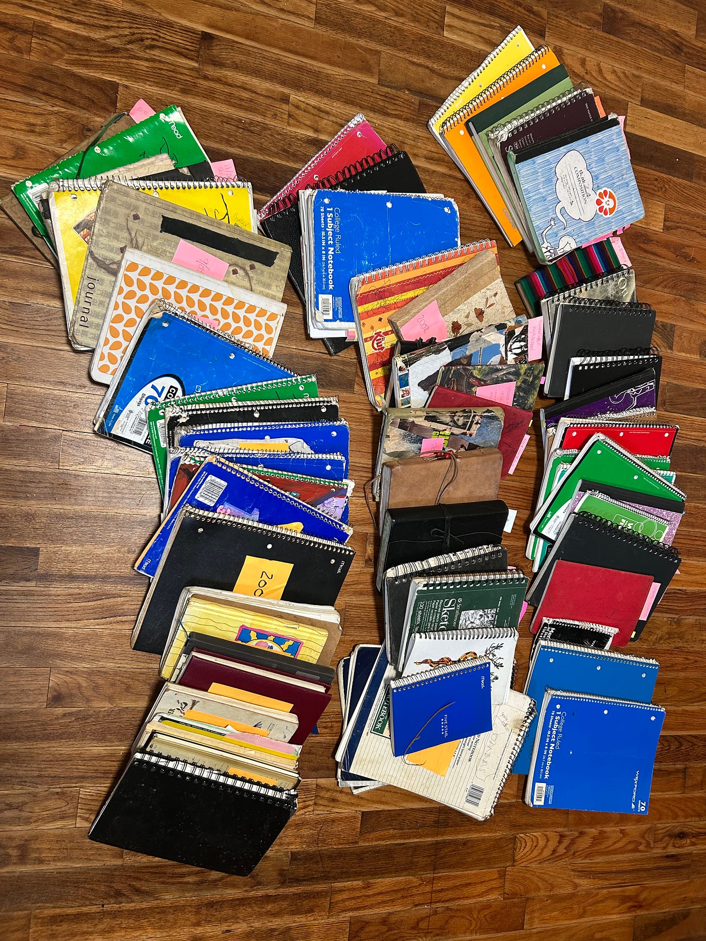 Three piles of notebooks laid out on a wood floor. These are the journals Sokol has written in over the years. 