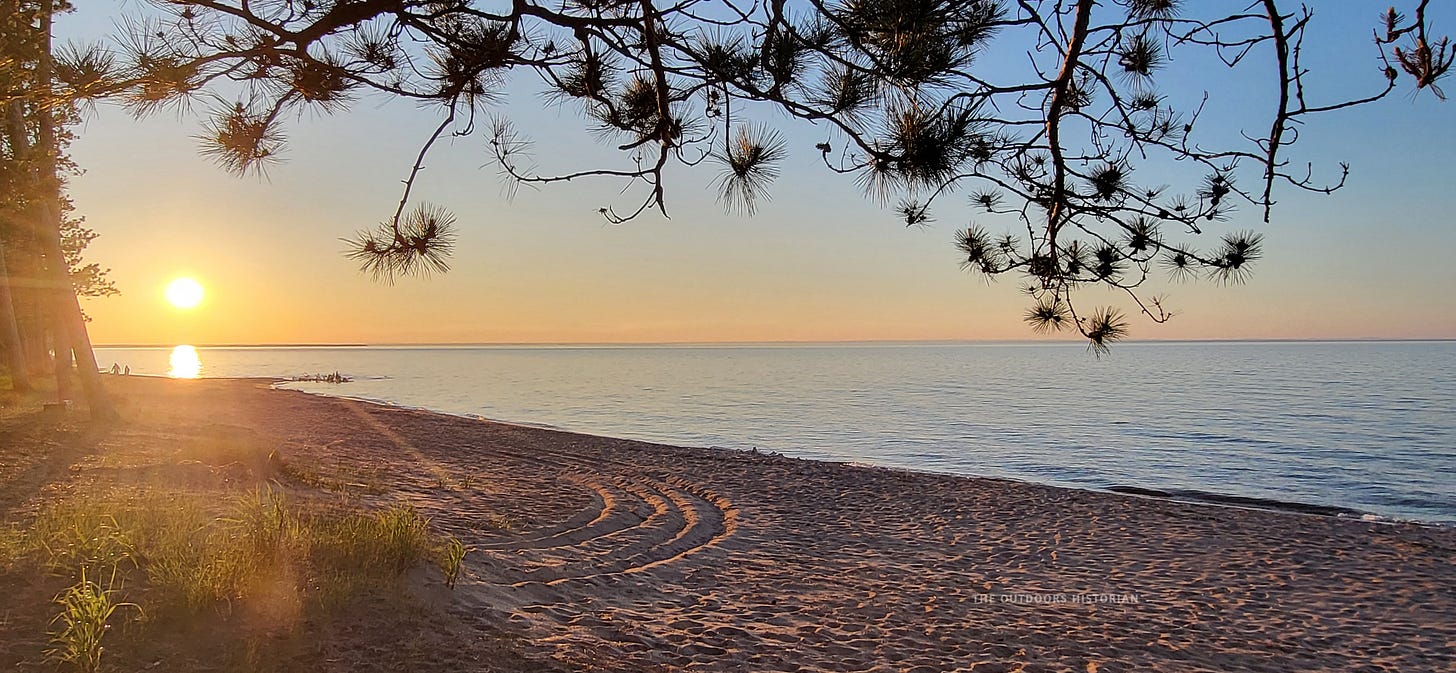 The sun rising over a sandy beach in the Keweenaw Peninsula, reflecting off the water.