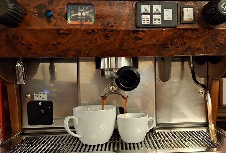 This may contain: two white coffee cups are being filled with liquid from the espresso machine,