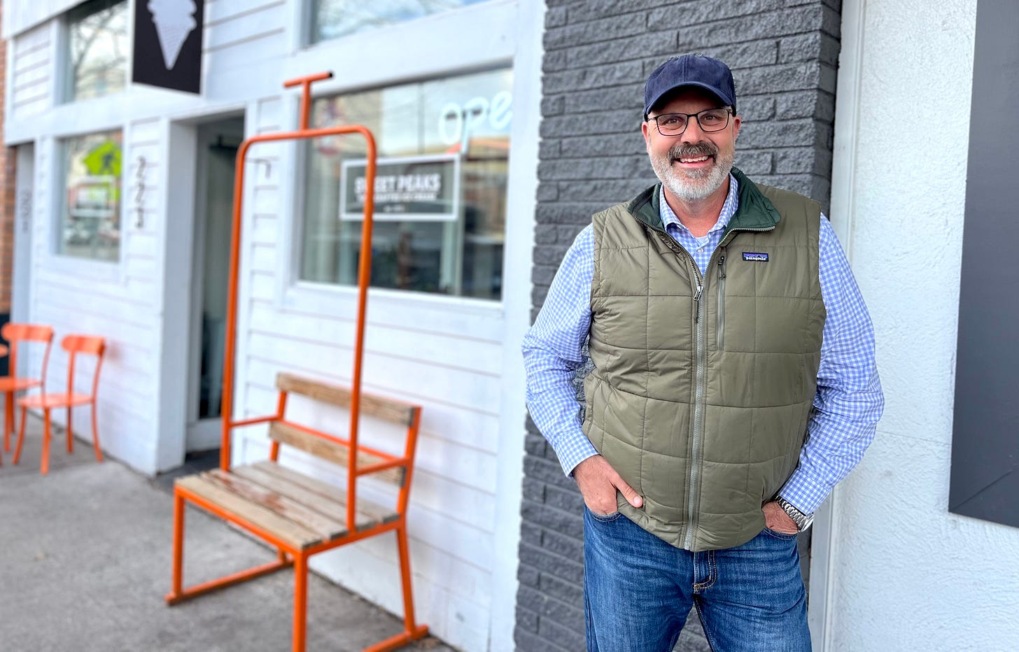 smiling man in green vest and jeans on city street