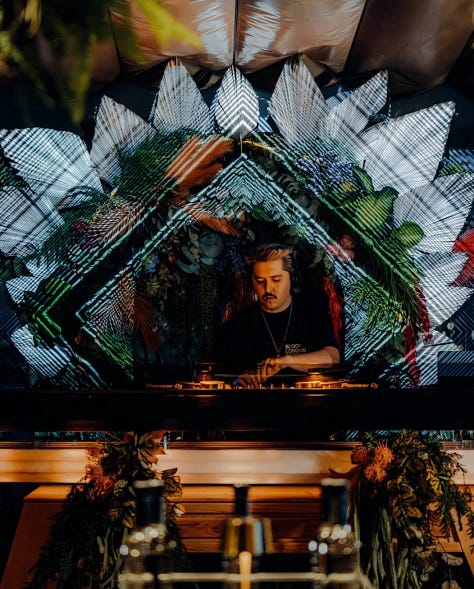Dj tocando, comida servida en la mesa y vista de una de las terrazas bar en CDMX desde las alturas.