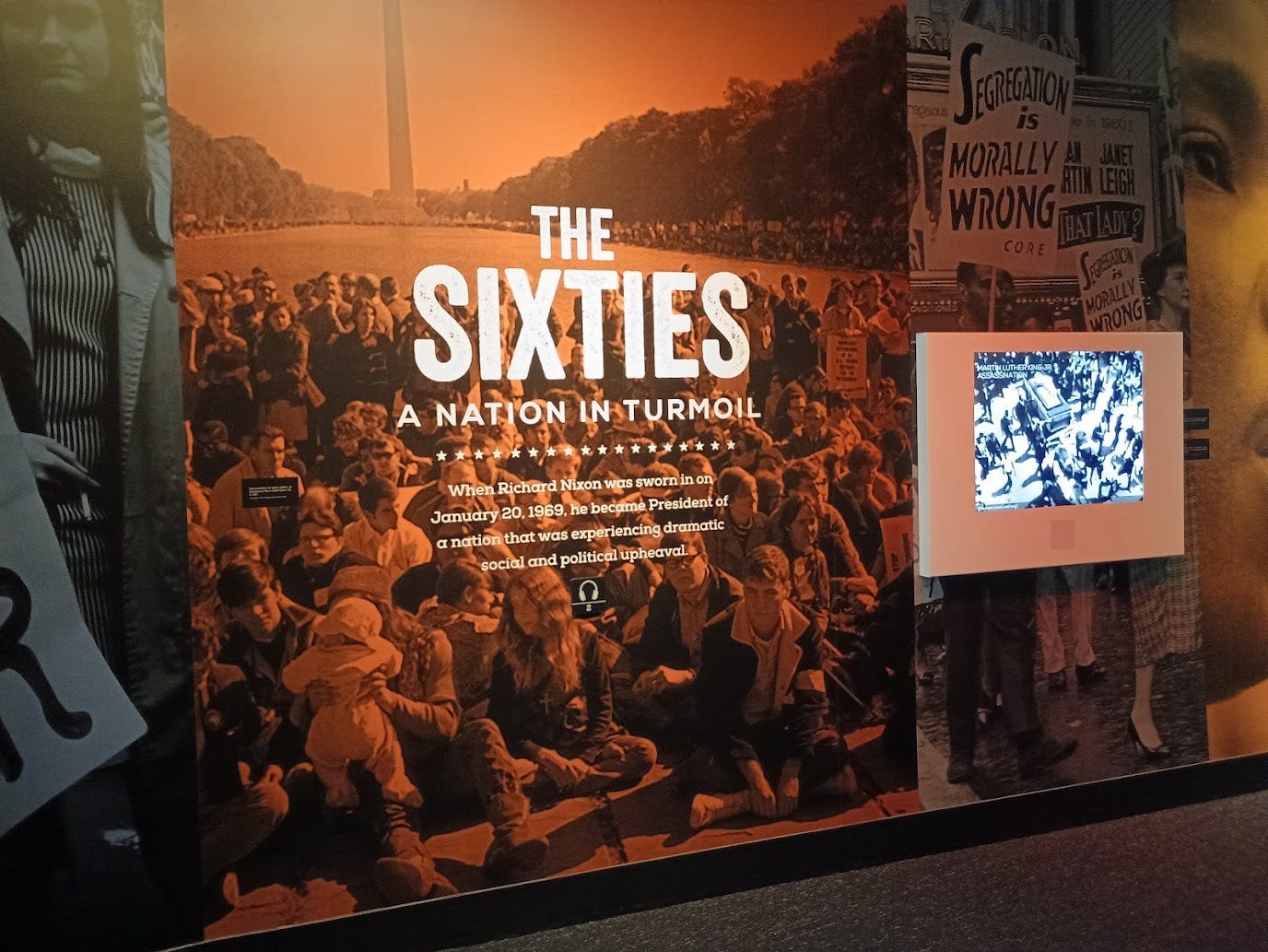 Picture of protestors by the reflecting pool on the National Mall, with a sign reading The Sixties