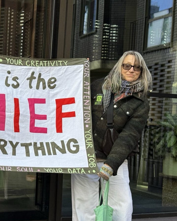 people stand outside office building holder a banner that reads "AI is the thief of everything"