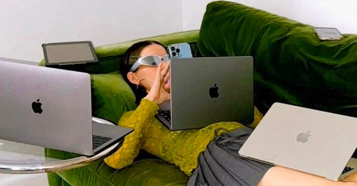 This may contain: a woman laying on a couch with two laptops