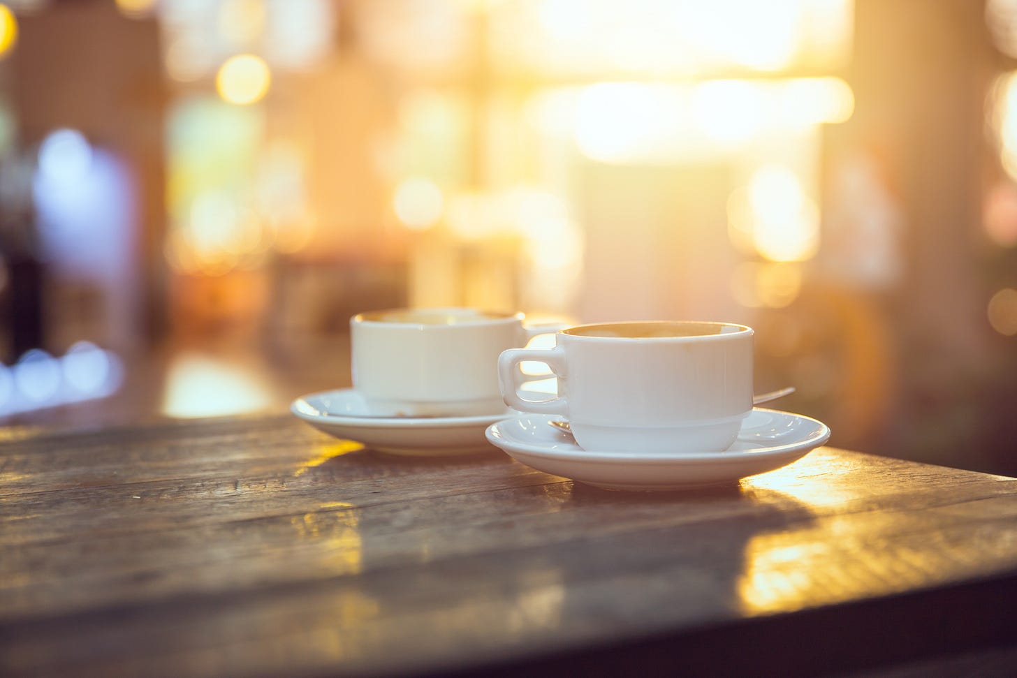 Two coffee cups on a table, softly out of focus, lit by warm afternoon light.