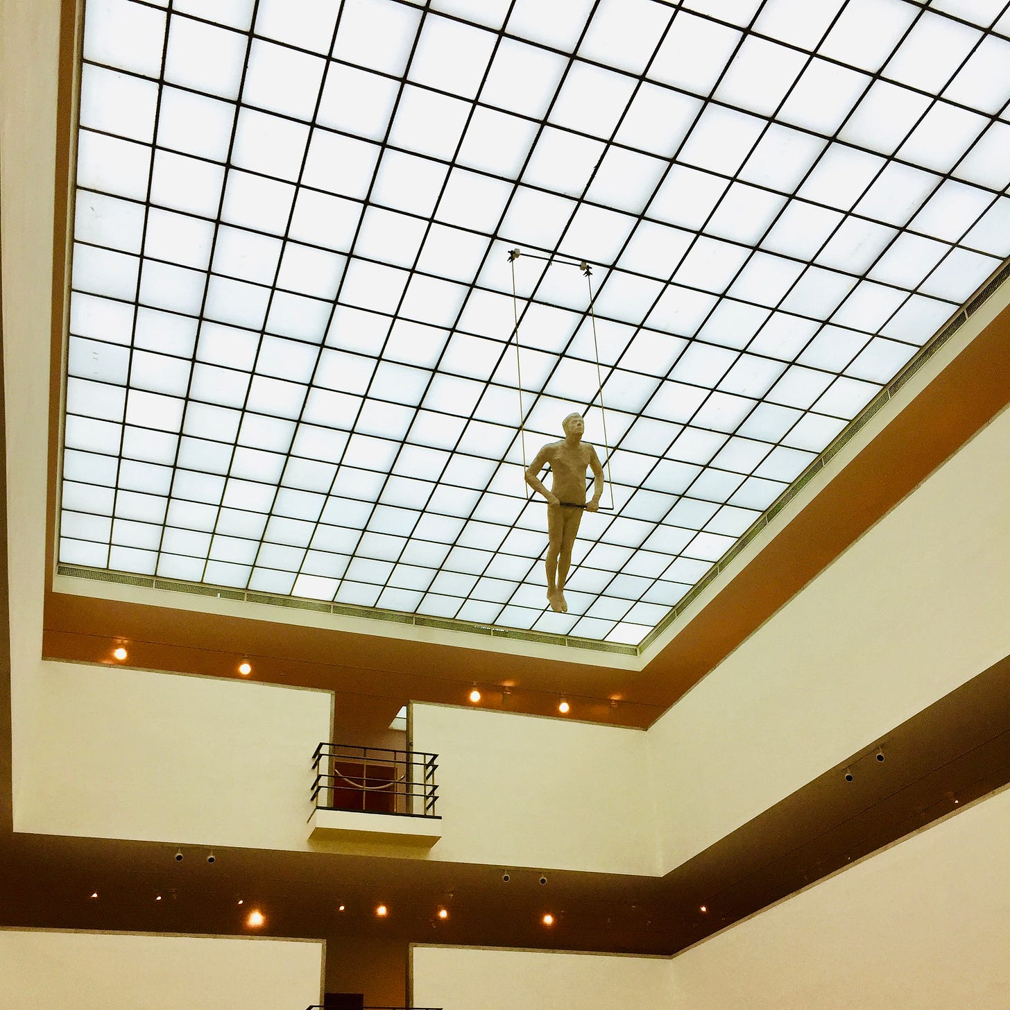 A statue of a trapeze artist hangs from an art museum ceiling