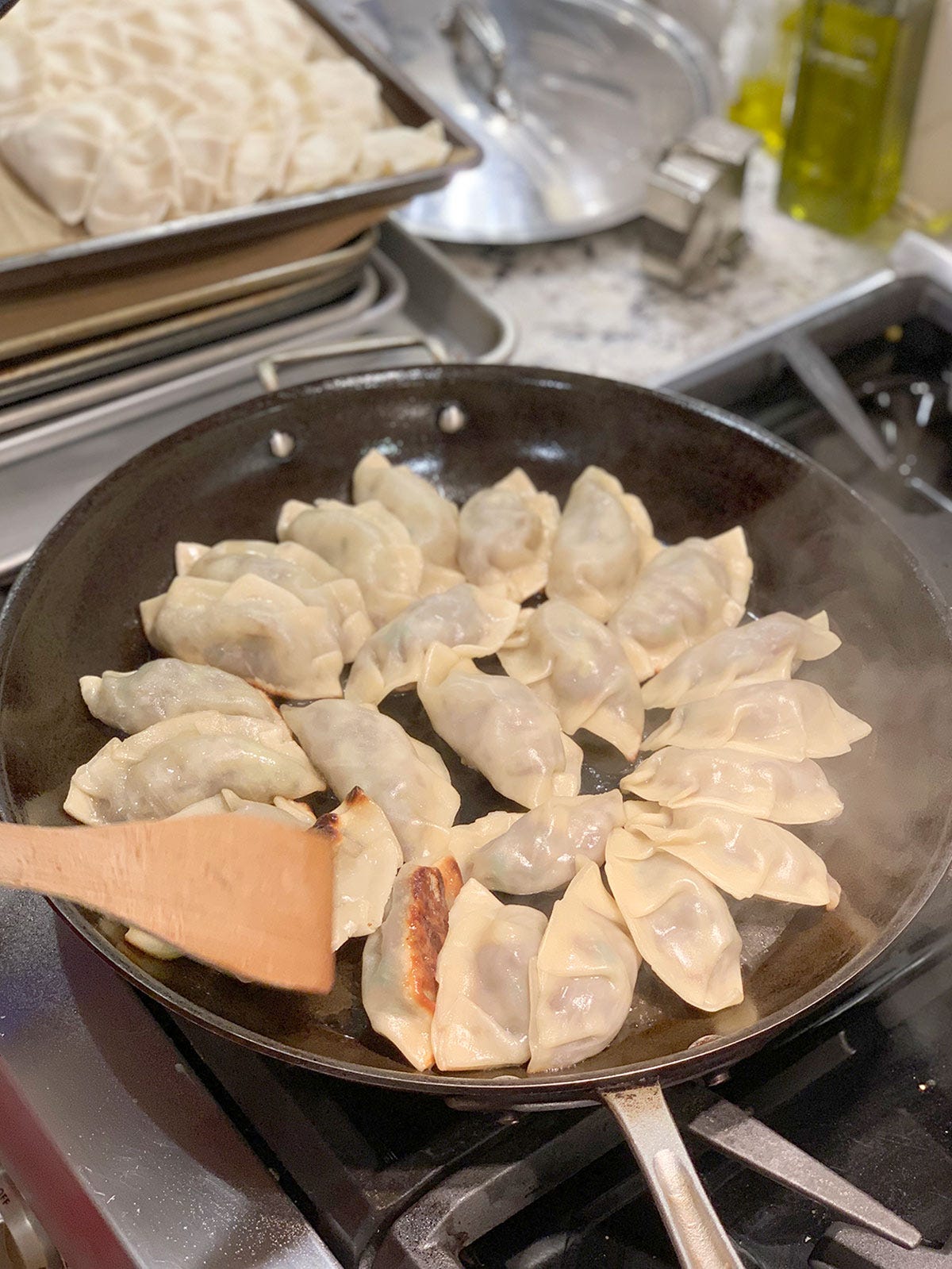 Mandu cooking in a large saute pan with a tray of mandu in the background.