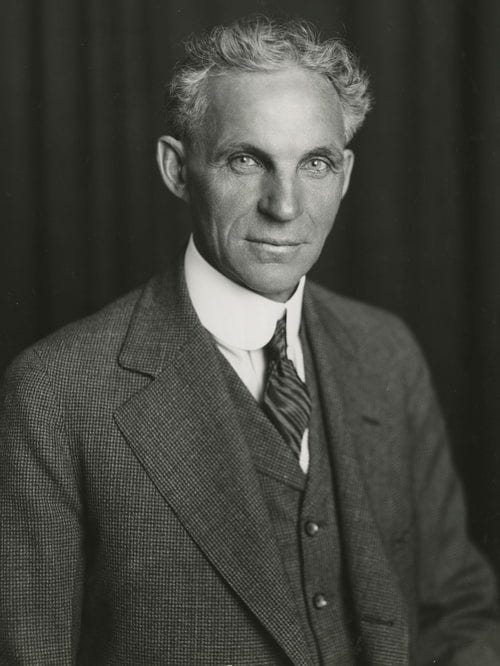 Studio portrait of Henry Ford from 1915. The black and white photo shows a man in a three piece suit with a high collar. He has short, wavy hair and piercing eyes. 