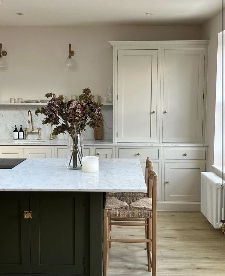 This may contain: a kitchen with white cabinets and marble counter tops, along with an island in the middle