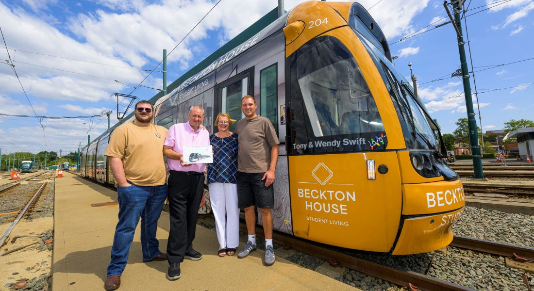 A group of people stood in front of a tram with a blue sky above them A group of people stood in front of a tram with a blue sky above them