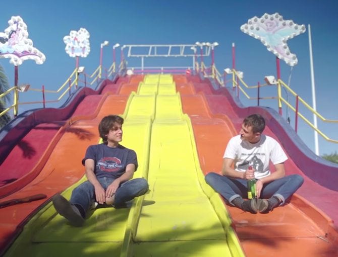 This may contain: two young men sitting on colorful slides at an amusement park