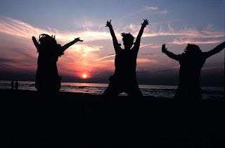 silhouette of three young people jumping joyously on a beach with sunset behind