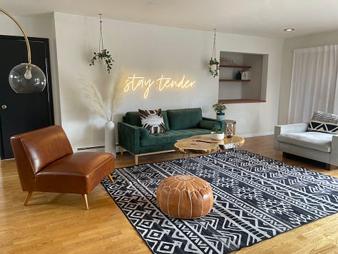 each photo is of Andrea and Meg's living room, painted in progressively different colors with slight alterations on decor at well. In first photo, wall is charcoal colored. Subsequently, emerald, light pink, wallpapered, white with a "stay tender sign", then white with a triptych of cacti.