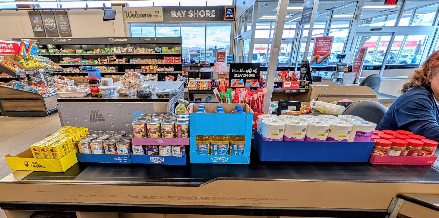 Grocery store checkout filled with canned goods, pasta, and pantry items being purchased for donation to a local food bank — a community member supporting neighbors during a time of food insecurity.