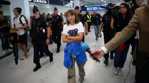 Reuters Swedish activist Greta Thunberg walks inside a terminal surrounded by journalists and French police at the Paris-Charles de Gaulle Airport.