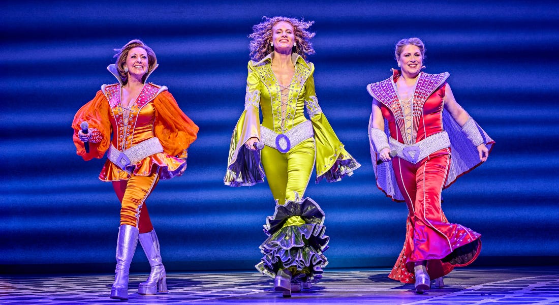 Three women on stage wearing colourful disco outfits Three women on stage wearing colourful disco outfits