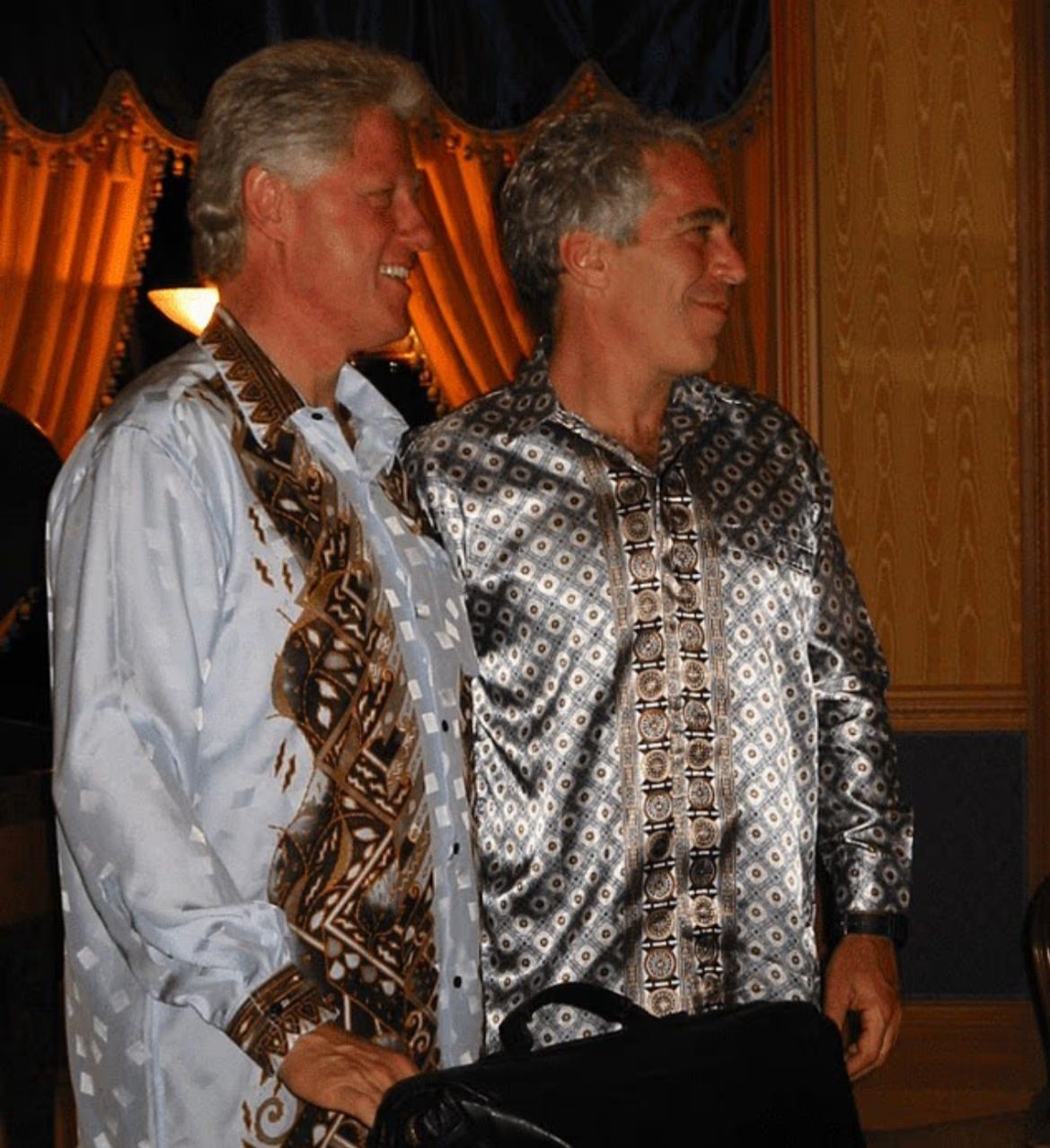 Two men in patterned shirts pose together in a well-decorated indoor setting with warm lighting.