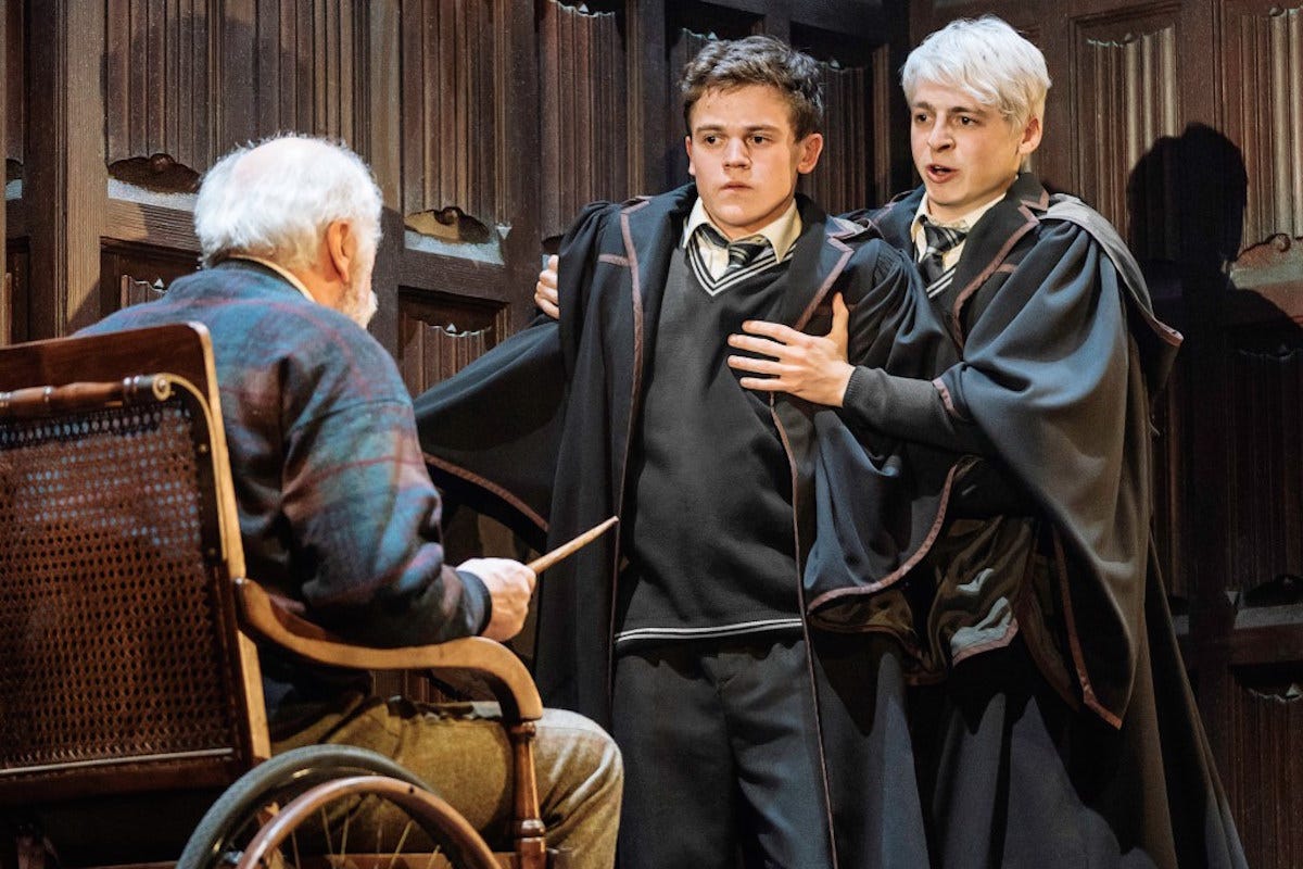 Two young male characters from the Harry Potter's universe, in school uniform, in shock, staring at an old man in a wheelchair pointing a wand at them.