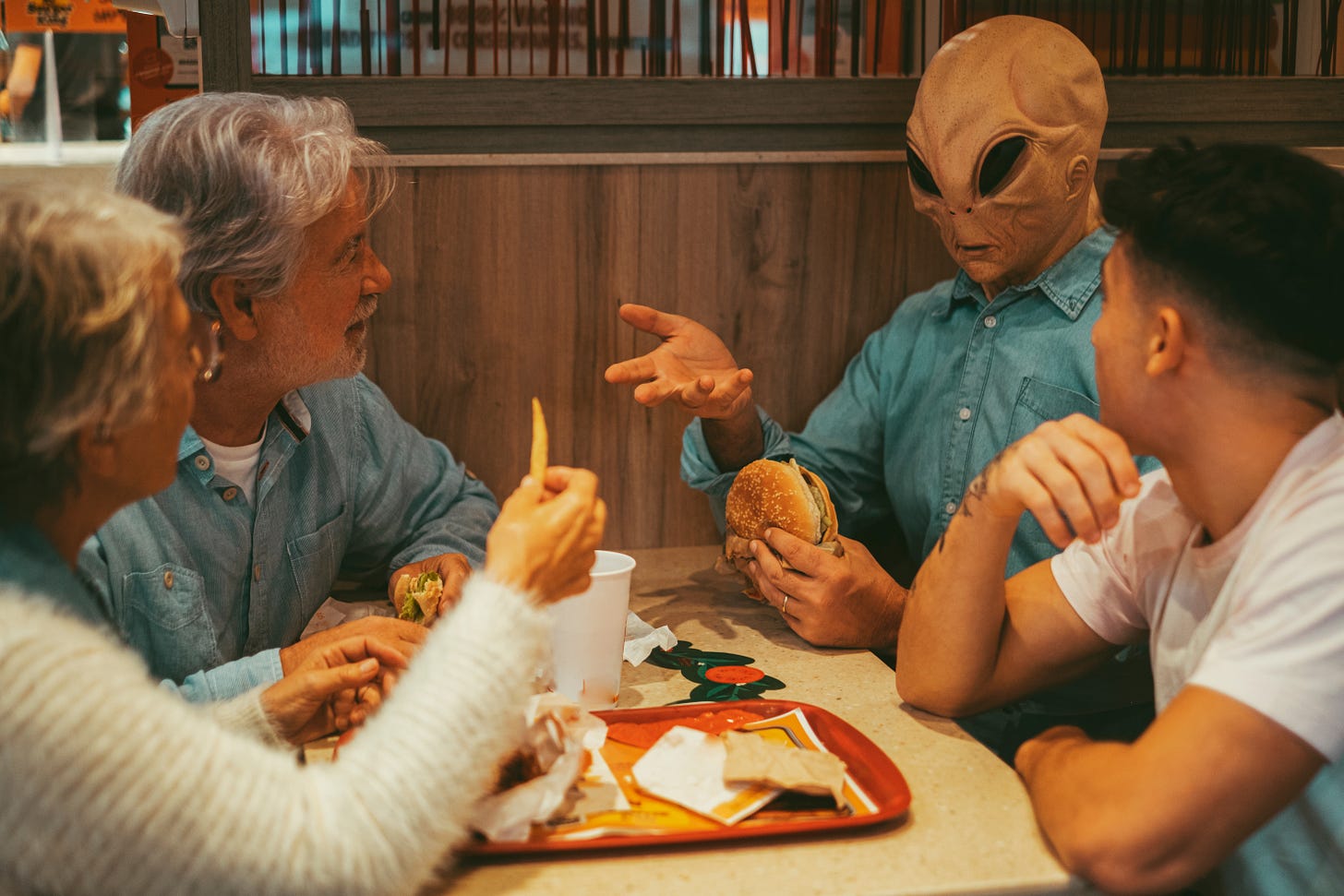 Three humans and an alien casually chatting in a fast food place Three humans and an alien casually chatting in a fast food place