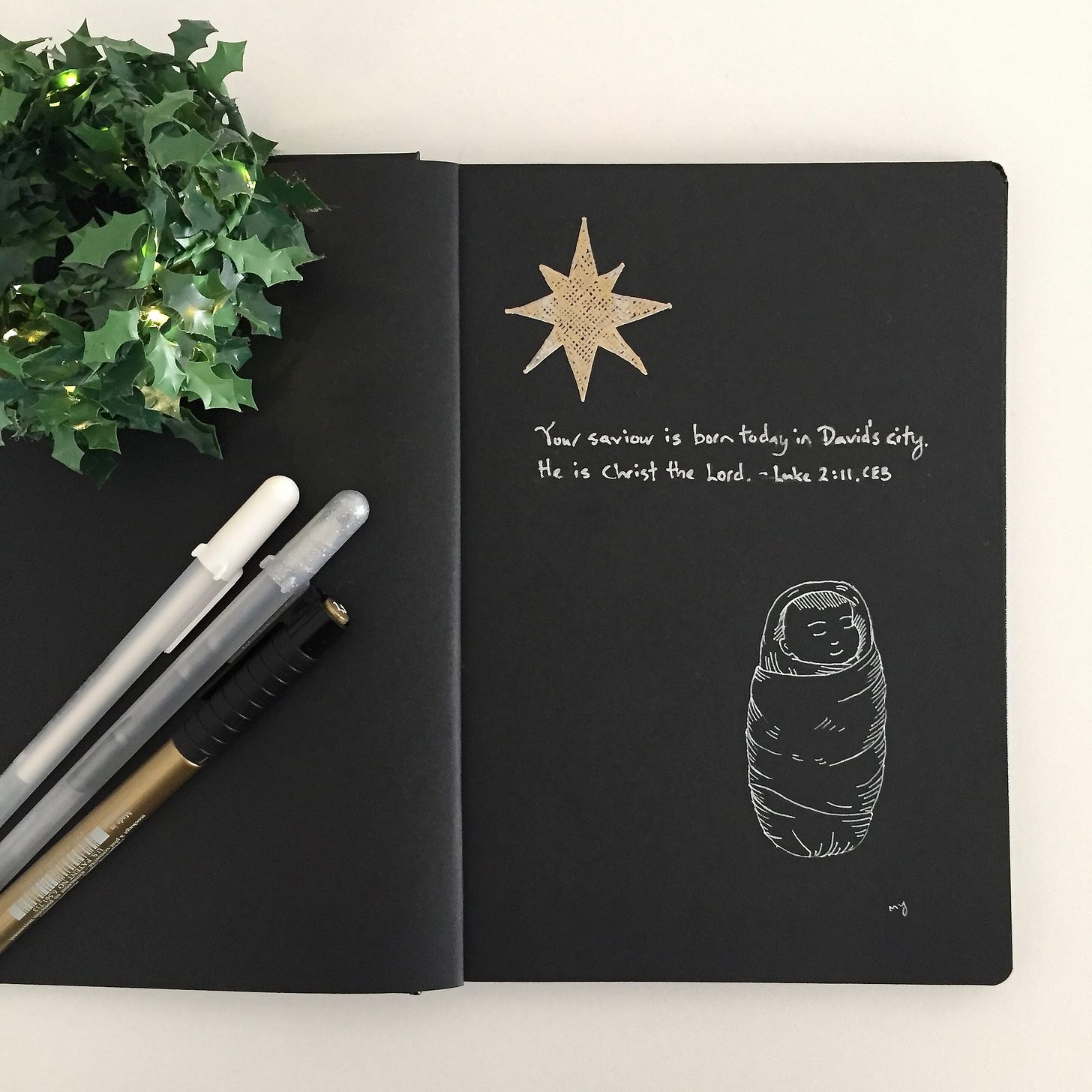 Line drawing with Bible verse Luke 2:11. Line drawing on black paper with white colour pen drawing of baby Jesus swaddled in cloth, sleeping peacefully. On the top left is a golden star of Bethelem. The Bible verse reads in silver colour, “Your saviour is born today in David’s city. He is Christ the Lord.” Luke 2:11 CEB