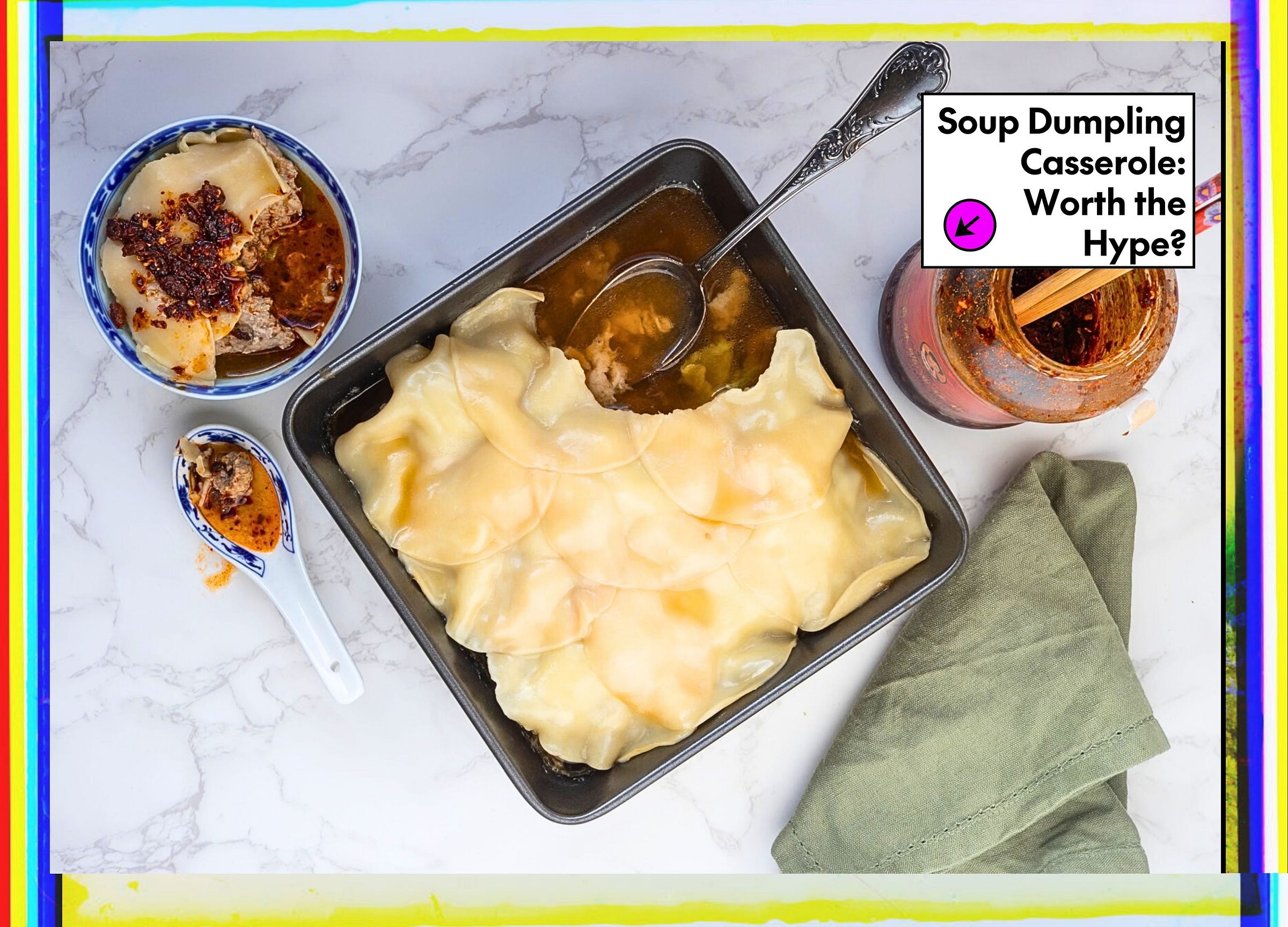 Overhead styled food photo of a soup dumpling casserole in a dark square pan with a ladle scooping golden broth. Accompanied by a blue and white bowl of dumplings with chili crisp, a soup spoon, a jar of chili oil with chopsticks, and a green linen napkin on a marble surface. A text overlay reads 'Soup Dumpling Casserole: Worth the Hype?'
