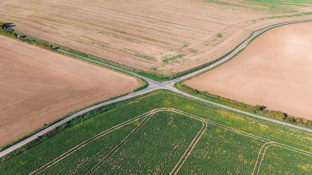 An aerial/drone view of a country road running through agricultural fields in the UK. There is a crossroads where 4 roads meet