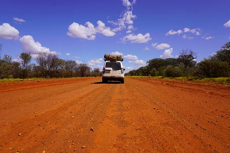 A collection of photos from an Australian outback expedition including a detailed travel map with route flags, a loaded 4WD vehicle on a red dirt road, and a sunset campsite in the desert.