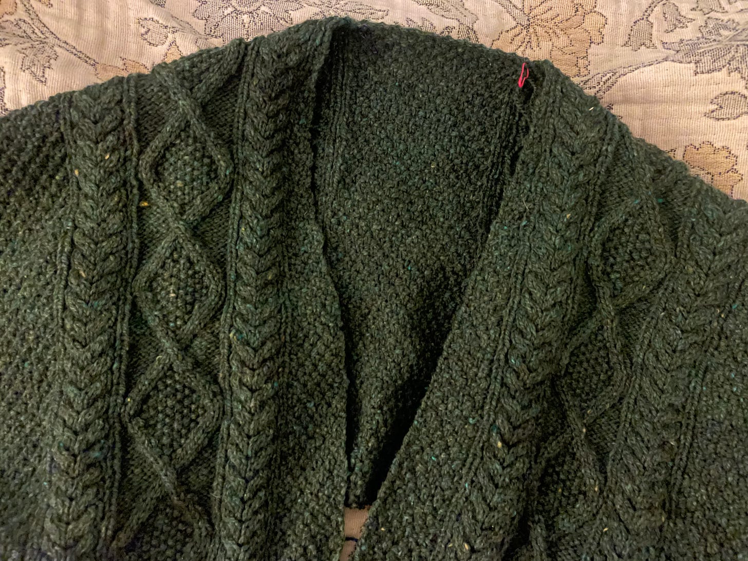 a close up of an in-progress forest green knitted cardigan. It is heavily cabled