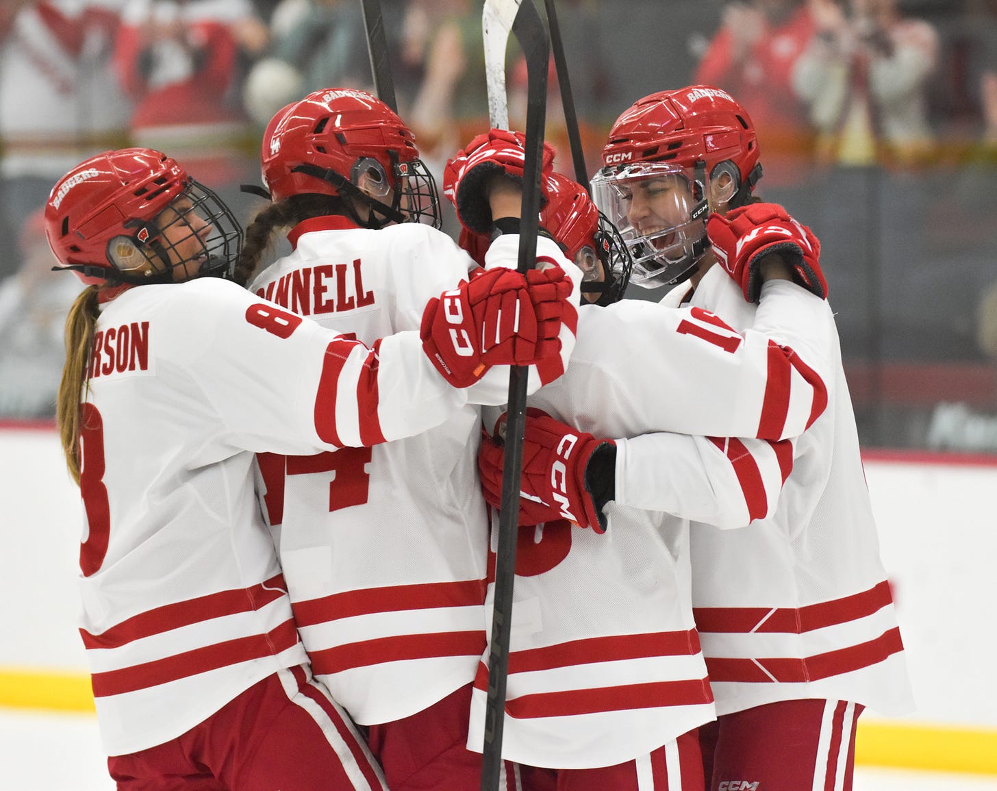 wisconsin women's hockey players huddle on the ice in celebration