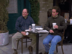 two men sit at a table with cups in their hands