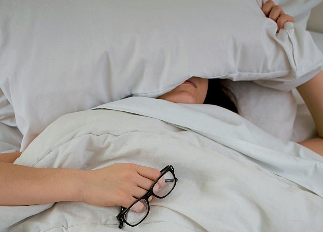 person lying on bed while covering face with pillow and holding eyeglasses person lying on bed while covering face with pillow and holding eyeglasses