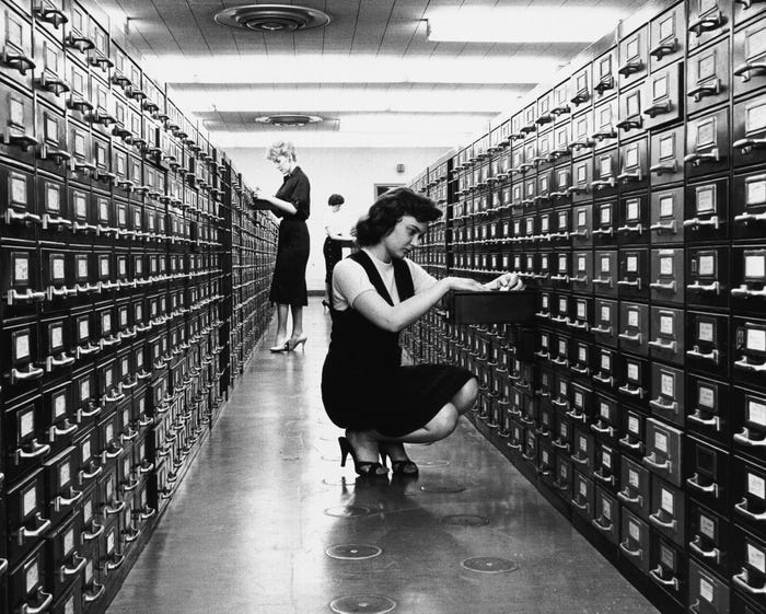 Three women, standing between two rows of filing cabinets, are consulting file cards and collecting information for the preparation of the new 'All Canadian Atlas', Ottawa, Ontario, Canada, 1959.