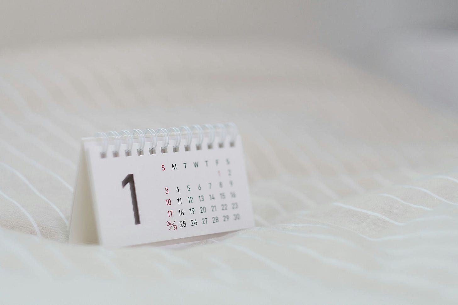 Desk calendar displaying the number "1" with visible weekdays on a soft, light-striped fabric background, creating a calm atmosphere. New beginnings