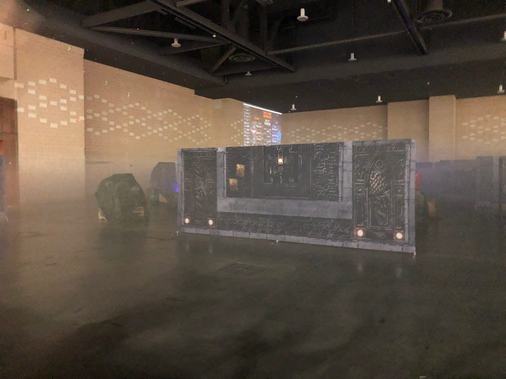 A banner painted with gothic iconography stands in the middle of a convention hall with concrete flooring and dense smoke.