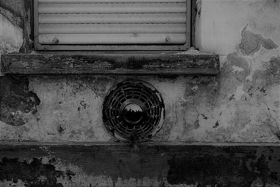 Grungy exterior wall with a vent and window shutter.