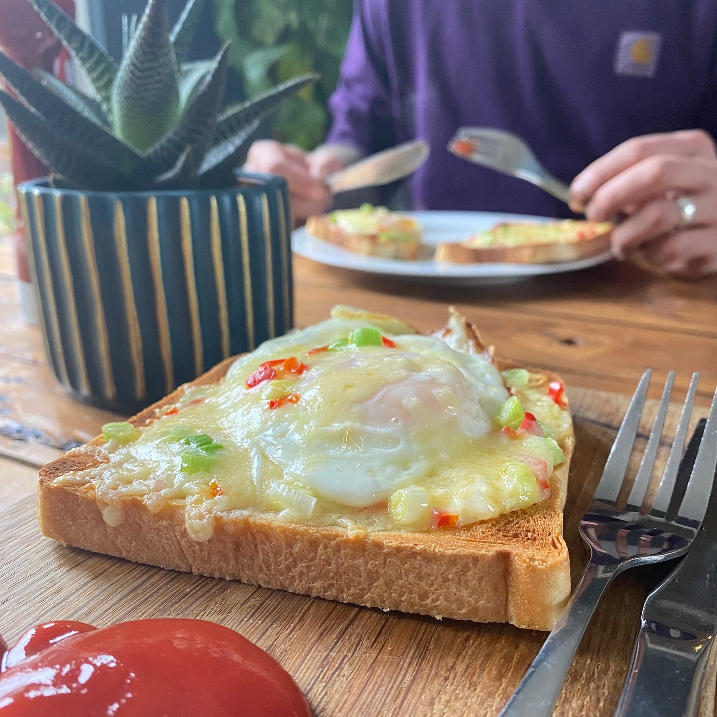 Slice of white bread topped with egg and cheese, a dollop of ketchup on a wooden board. 