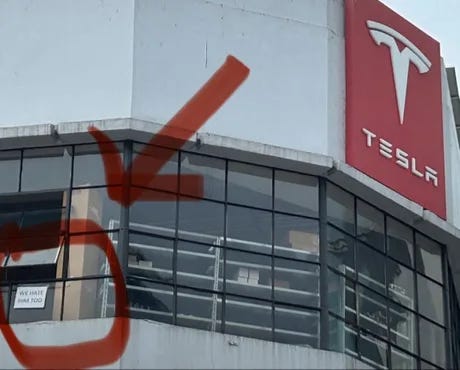 A sign posted in the window of a Tesla office that reads, “We hate him too”