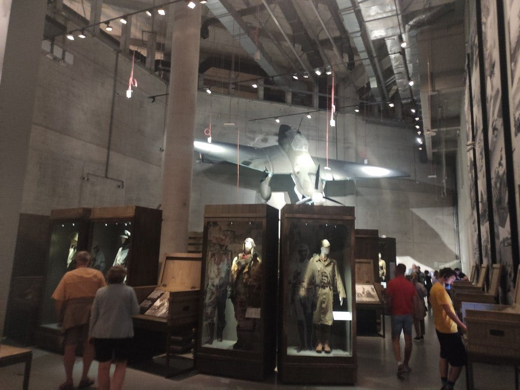 A large hall, with military uniforms, half a plane 'dive bombing' from the wall and computer screens against the wall
