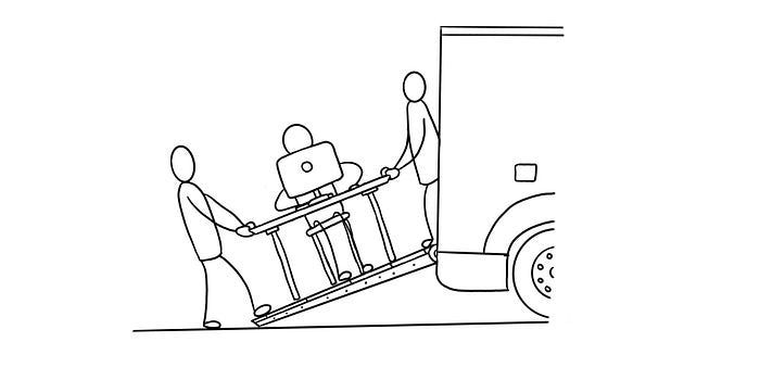 Two people carrying a designer who is still sitting at the desk working on their computer. People are putting the designer and desk in a truck.