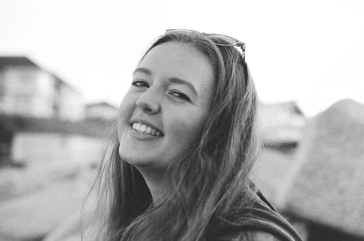 Guest author Rebecca Hooper in black-and-white, smiling at the camera, an out-of-focus seascape and beach houses in the background