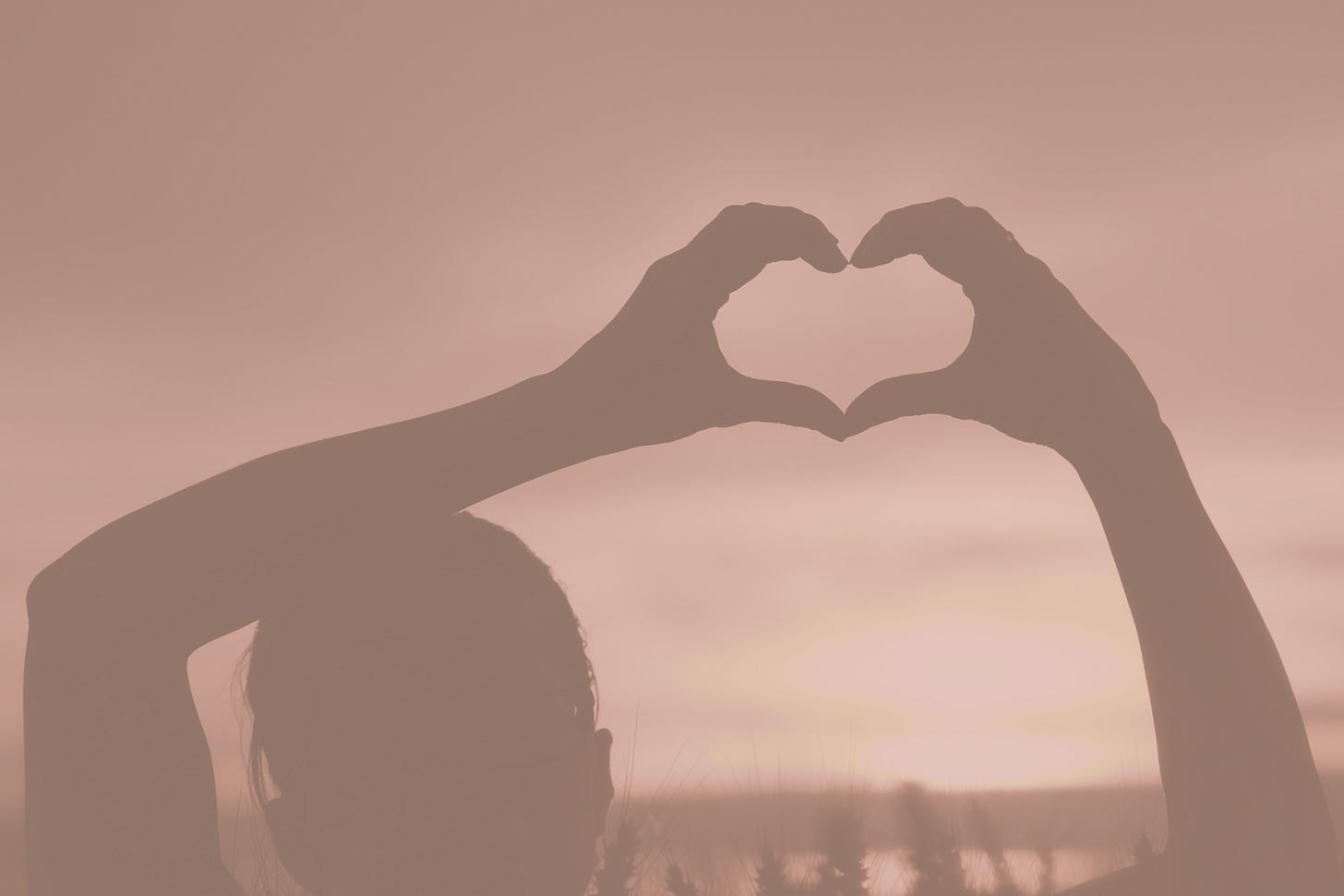 Person's silhouette raising hands in a heart shape