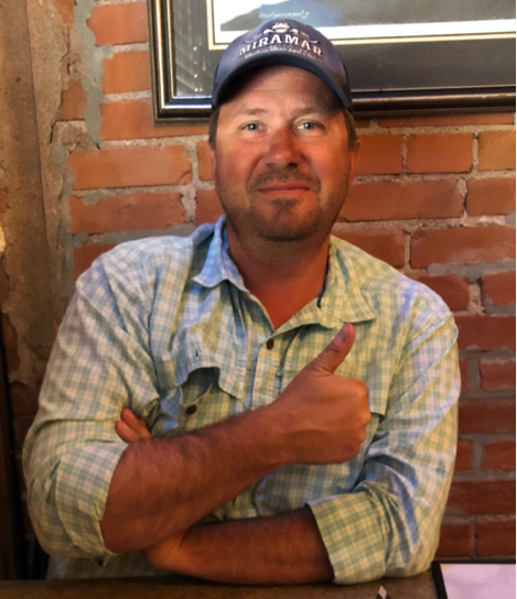 A person wearing a baseball cap giving a thumbs up

Description automatically generated